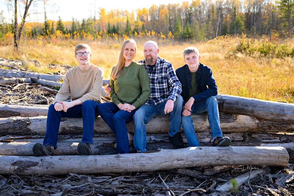 Family of four posing on logs in fall background
