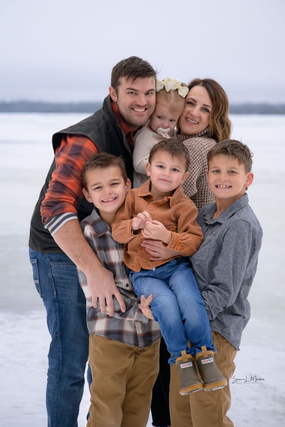 Young family of five cuddling with lake in background