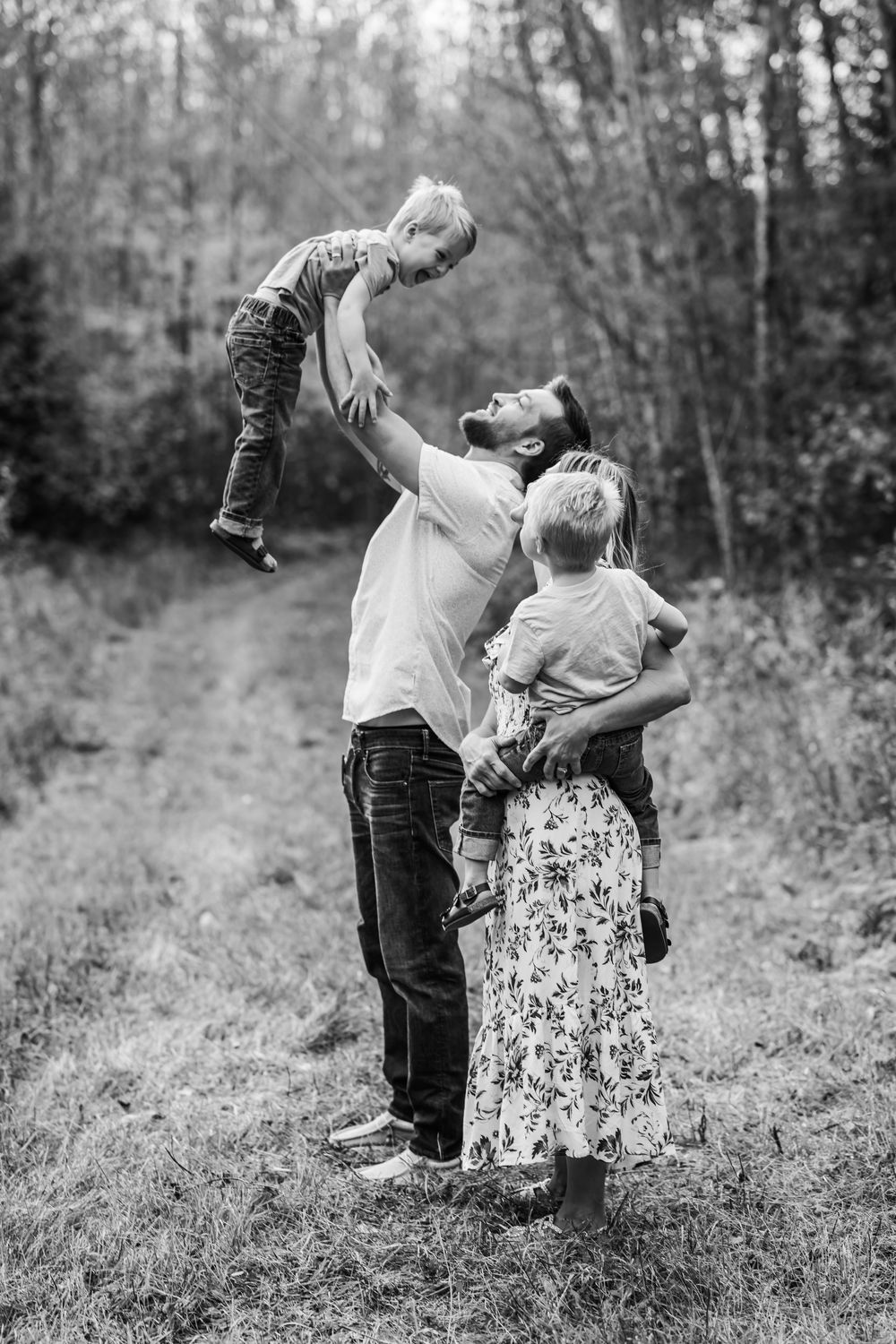 family of four posing with father holding son high up in air in black and white