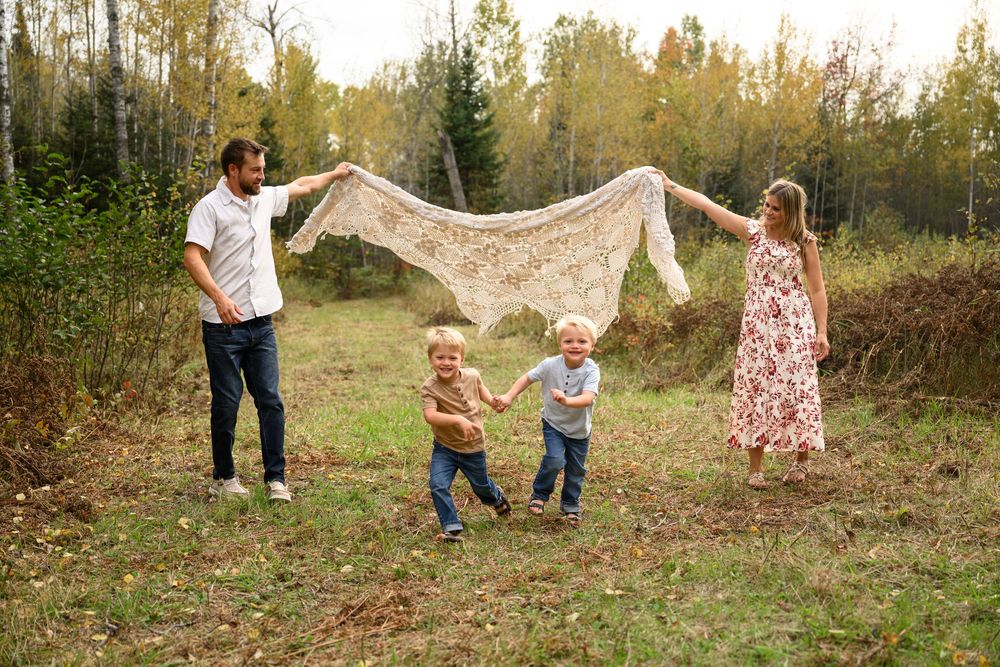 Family of 4 with parents holding blanket with children running under