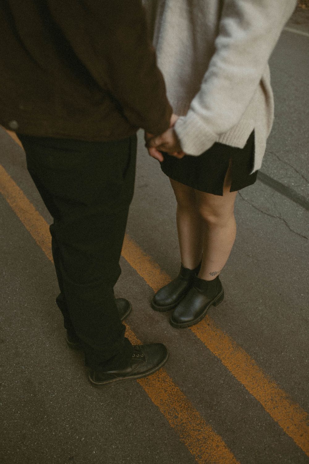 Couple holding hands on a road, woman wearing black skirt and ankle boots.