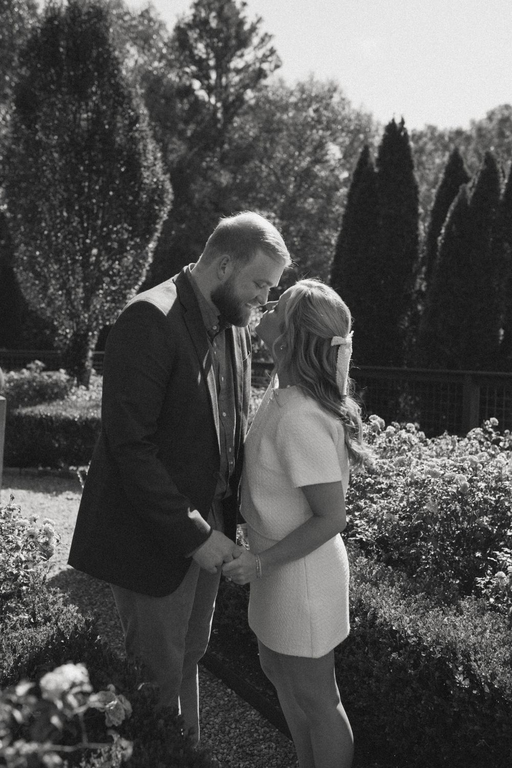 Black and white photo of a couple holding hands and sharing a romantic moment in a lush garden.