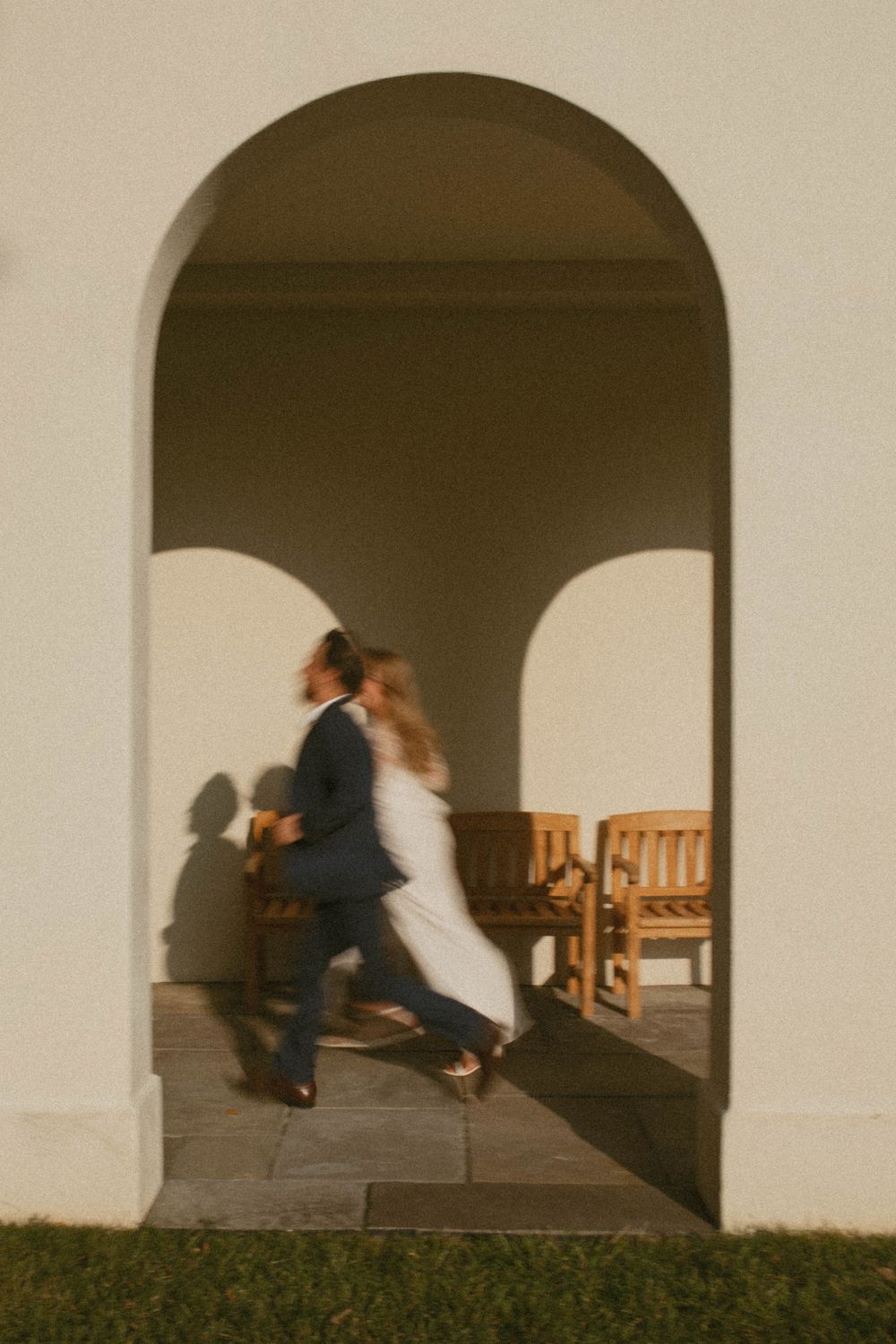 Couple in formal attire walking through an arched doorway at golden hour.