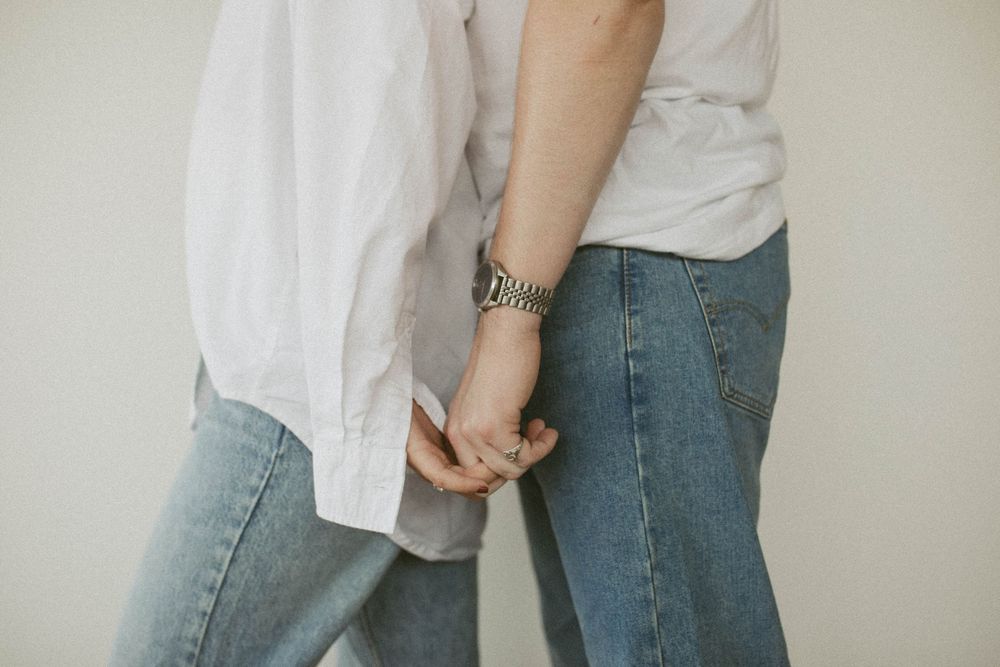 Close-up of a couple holding hands, both wearing jeans and white tops with a silver watch visible.