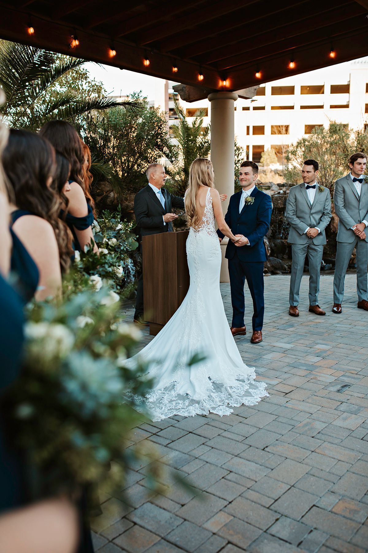 Couple exchanges vows during outdoor wedding ceremony under pergola with string lights and lush greenery in Roseville.