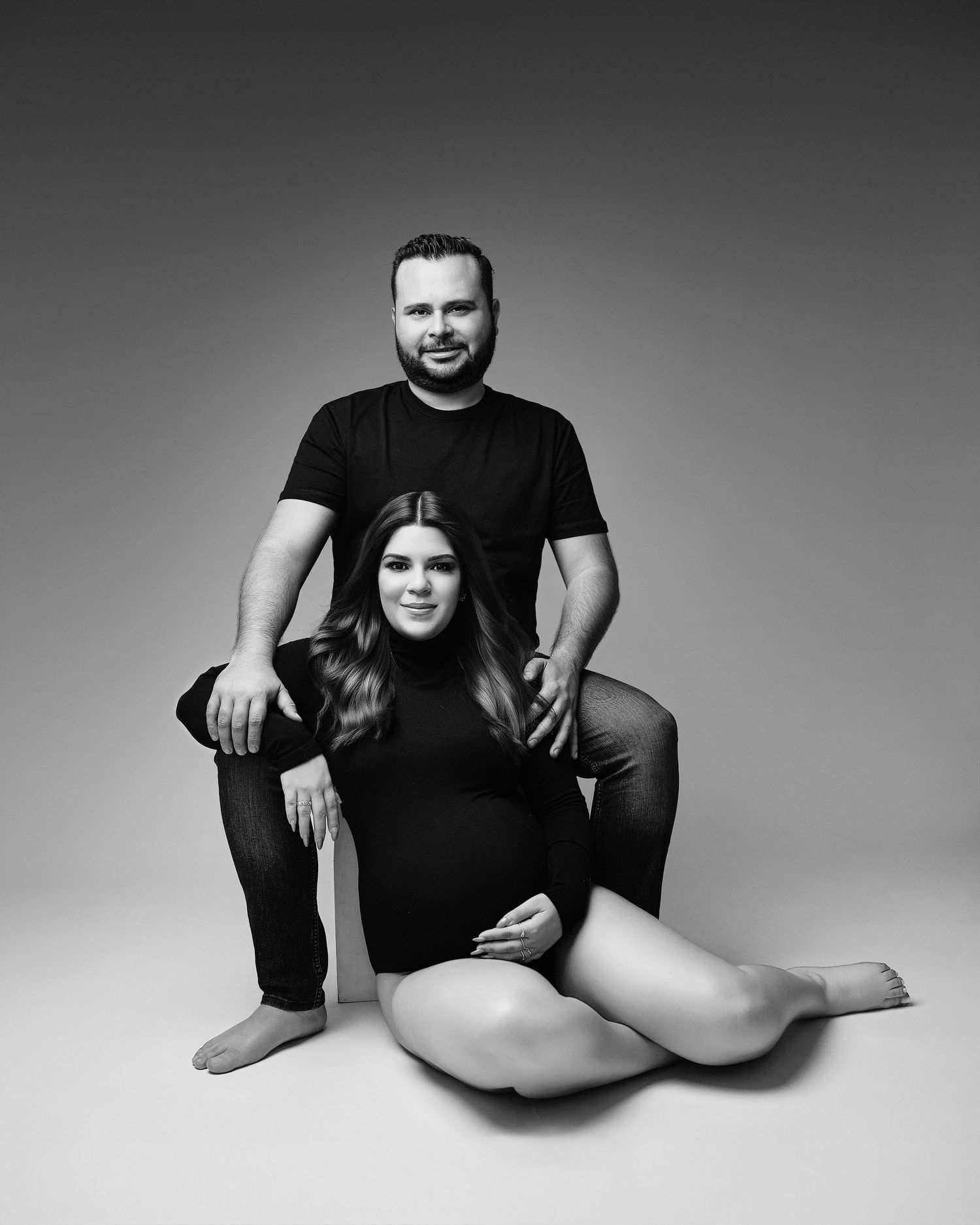 Black and white studio photograph showing artistic silhouettes of nude bodies with minimal shadows and backdrop.
