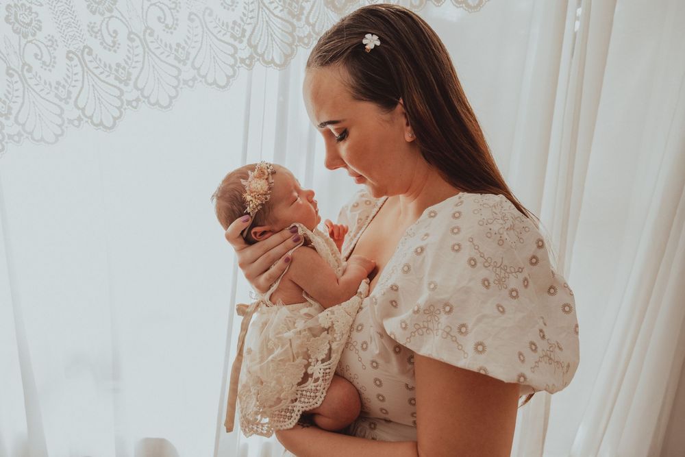 A tender moment between mother and baby as they share affectionate smiles while dressed in white lace outfits.