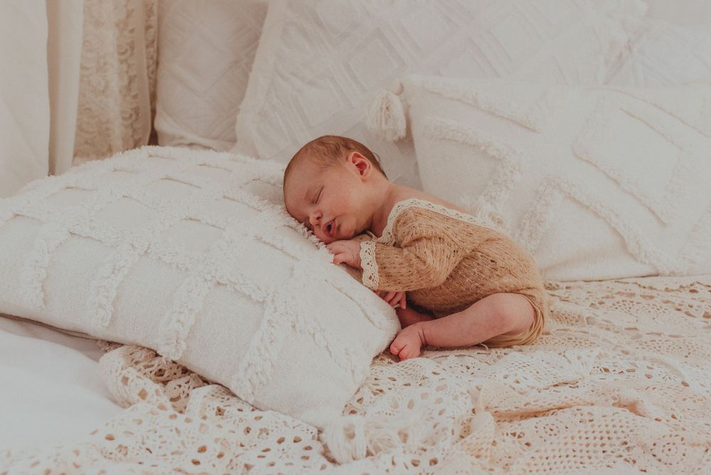 A sleeping baby in white bedding creates a peaceful scene with scattered delicate flowers decorating the background.