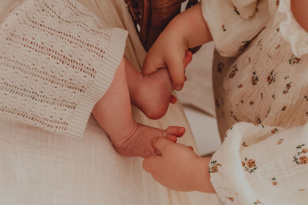 Tiny baby hands reach out and touch soft white floral fabric next to sheet music paper.