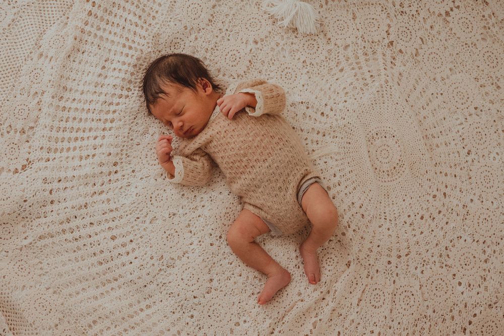 Peaceful sleeping baby lying on delicate lace blanket with soft beige tones during newborn photo session.