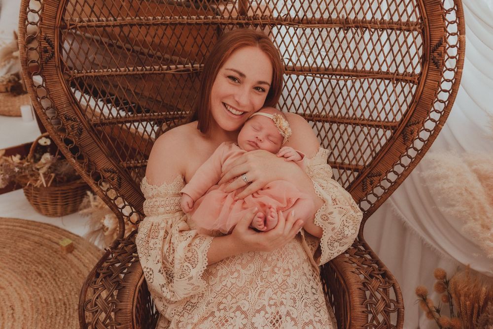 A peaceful moment captured in a wicker peacock chair with a sleeping newborn in a lace dress.