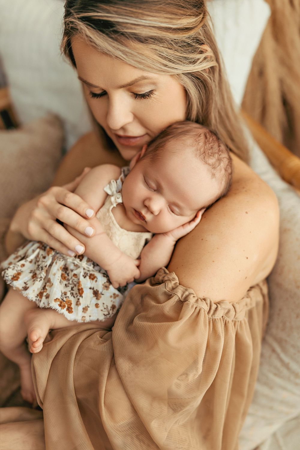 Tender moment between parent and sleeping newborn in soft warm lighting during professional photoshoot.