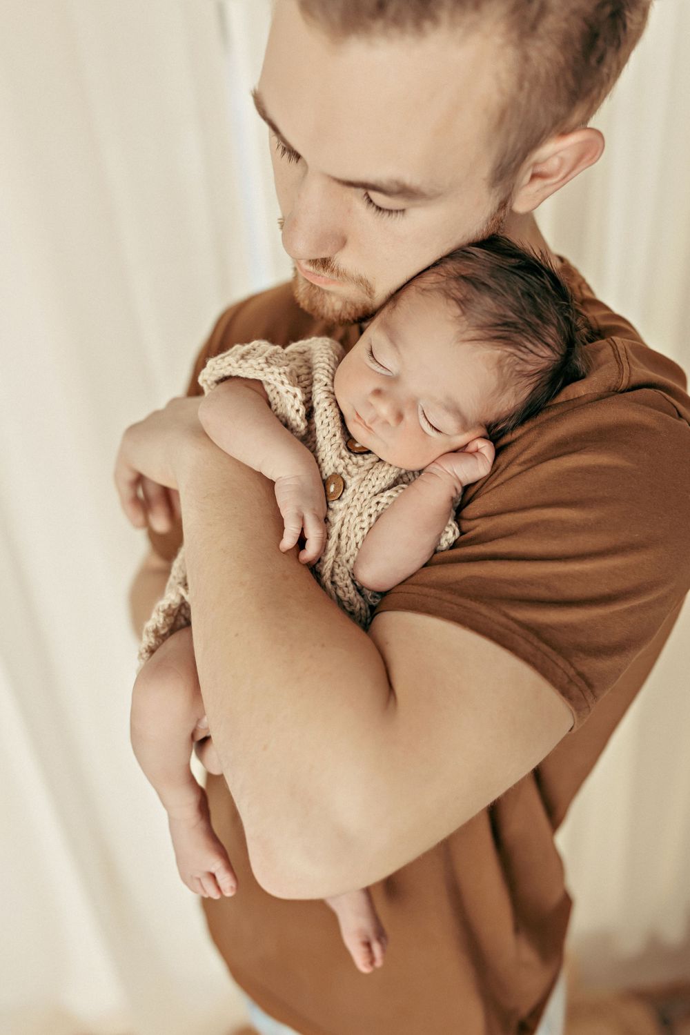 Tender moment between parent and sleeping newborn in cozy indoor setting.
