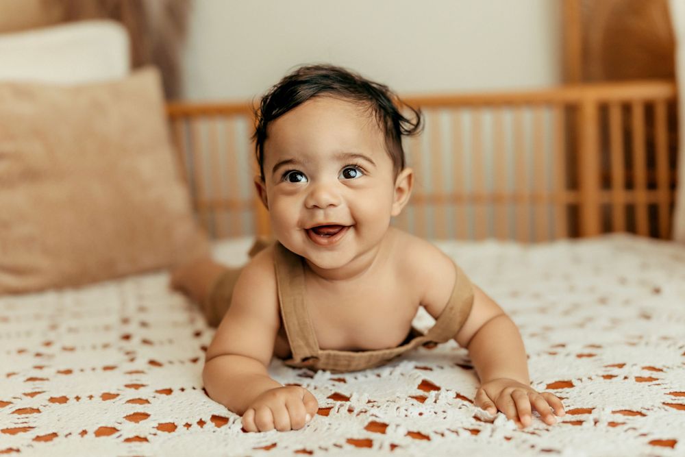 Happy baby lying on white lace blanket with big smile.