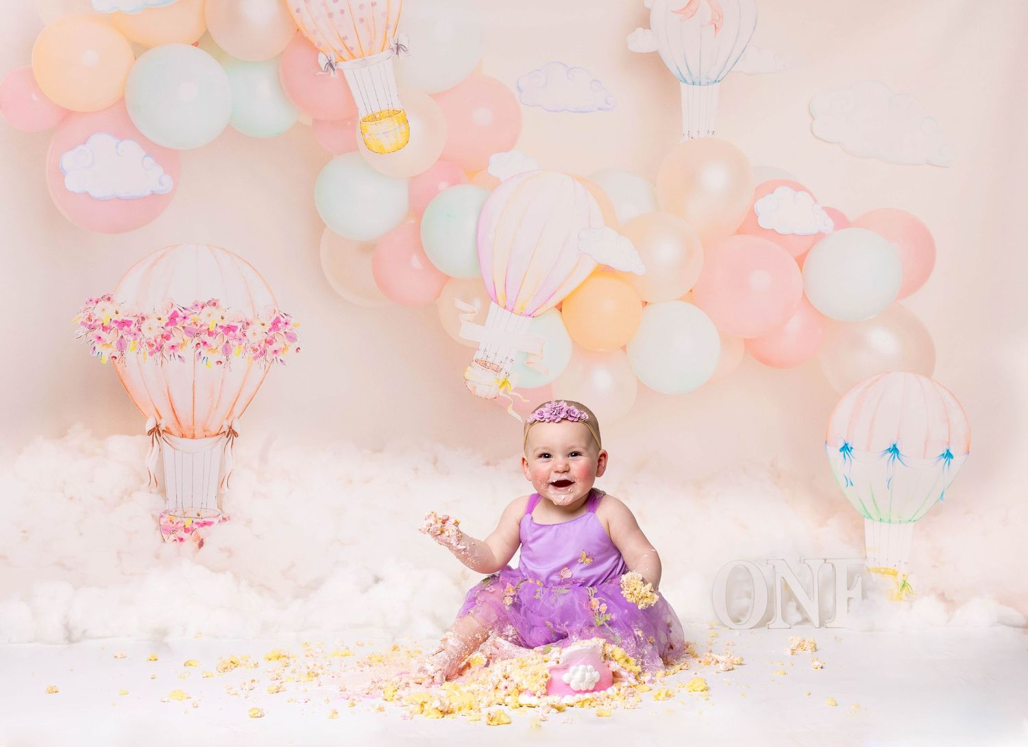 Baby during hot air balloon-themed cake smash in Chicago IL studio with pastel balloons, dreamy decor, and matching cake for first birthday