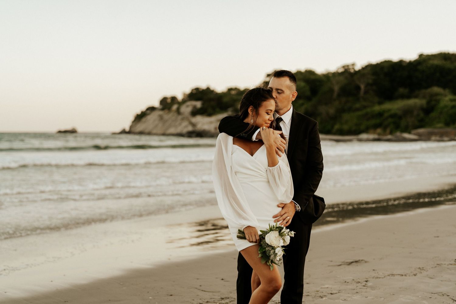 Couple walks hand in hand along a serene beach at sunset.