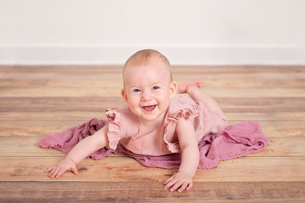 six month sitter session Baltimore Ontario. Baby girl lays on tummy pushing up on her hands in pink romper.*