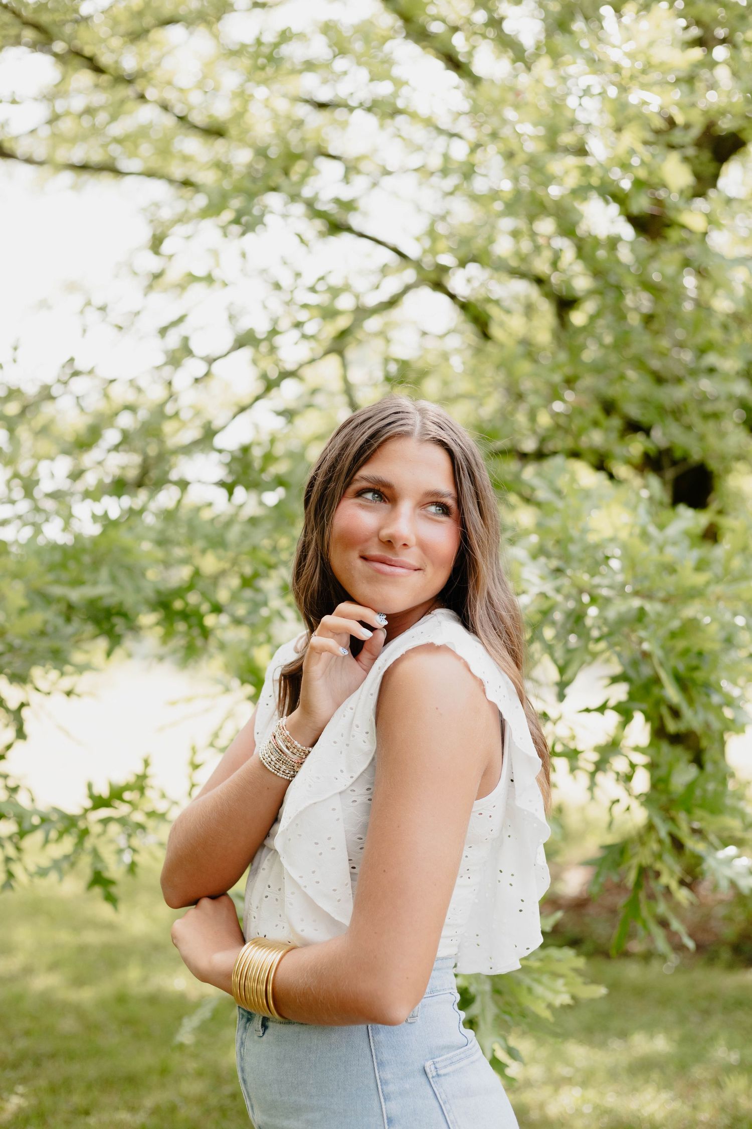Portrait of woman in white top posing against blooming spring tree branches.