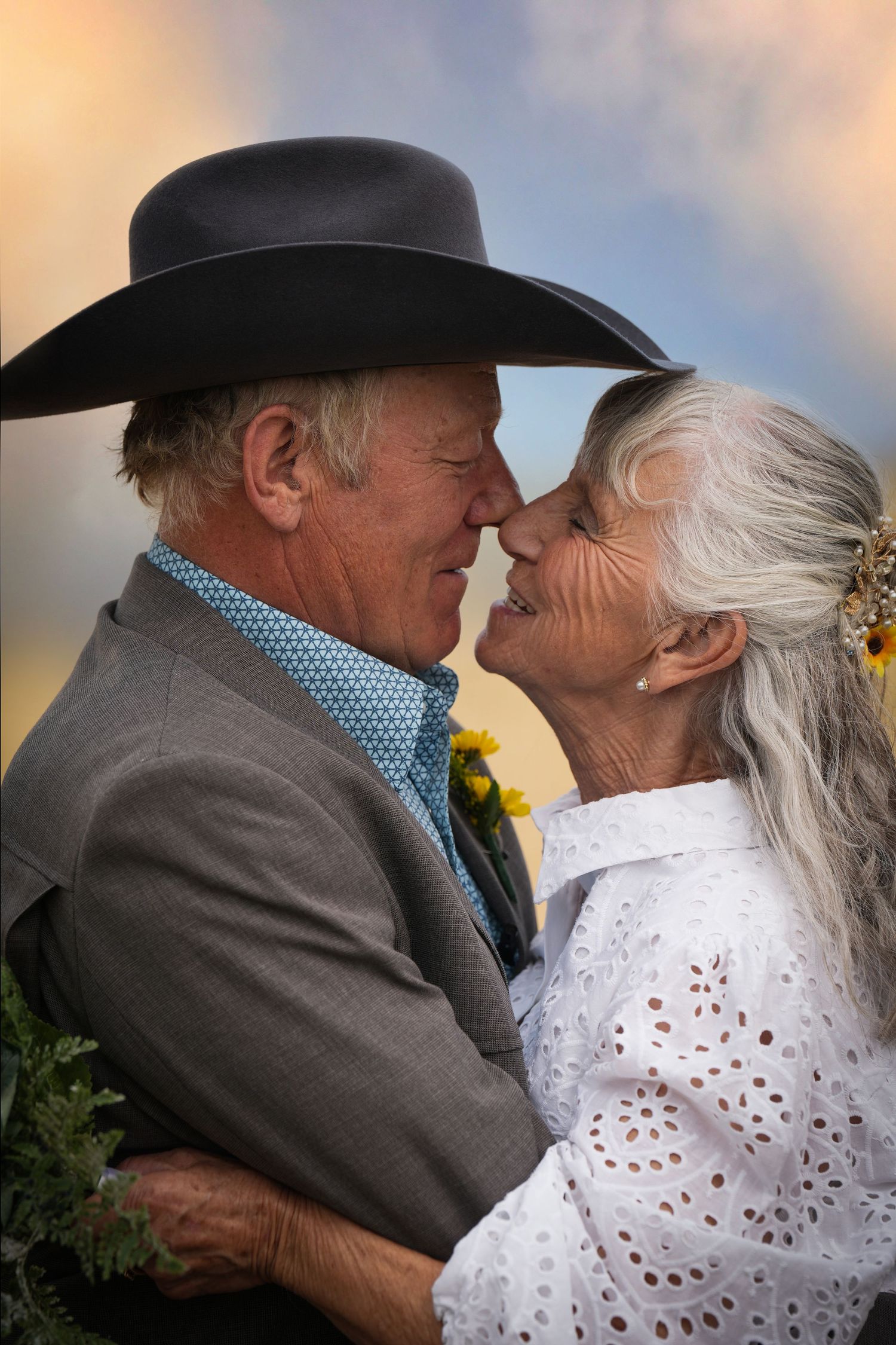 Tender moment between a couple in western attire against a sunset backdrop.