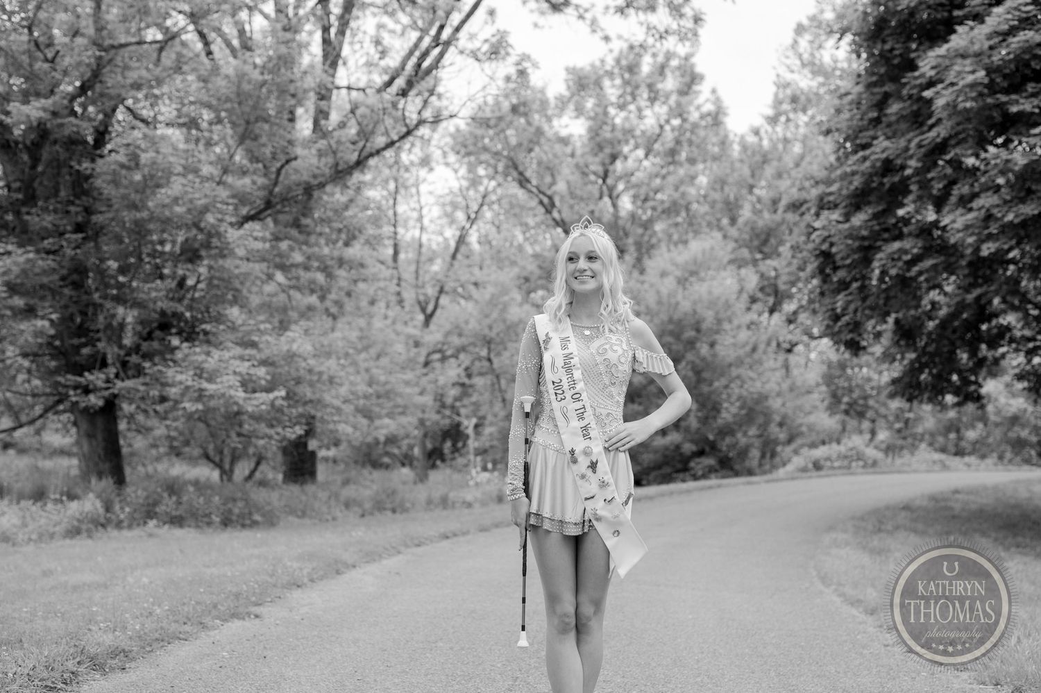 Black and white portrait of a person in a floral dress standing on a path outdoors.