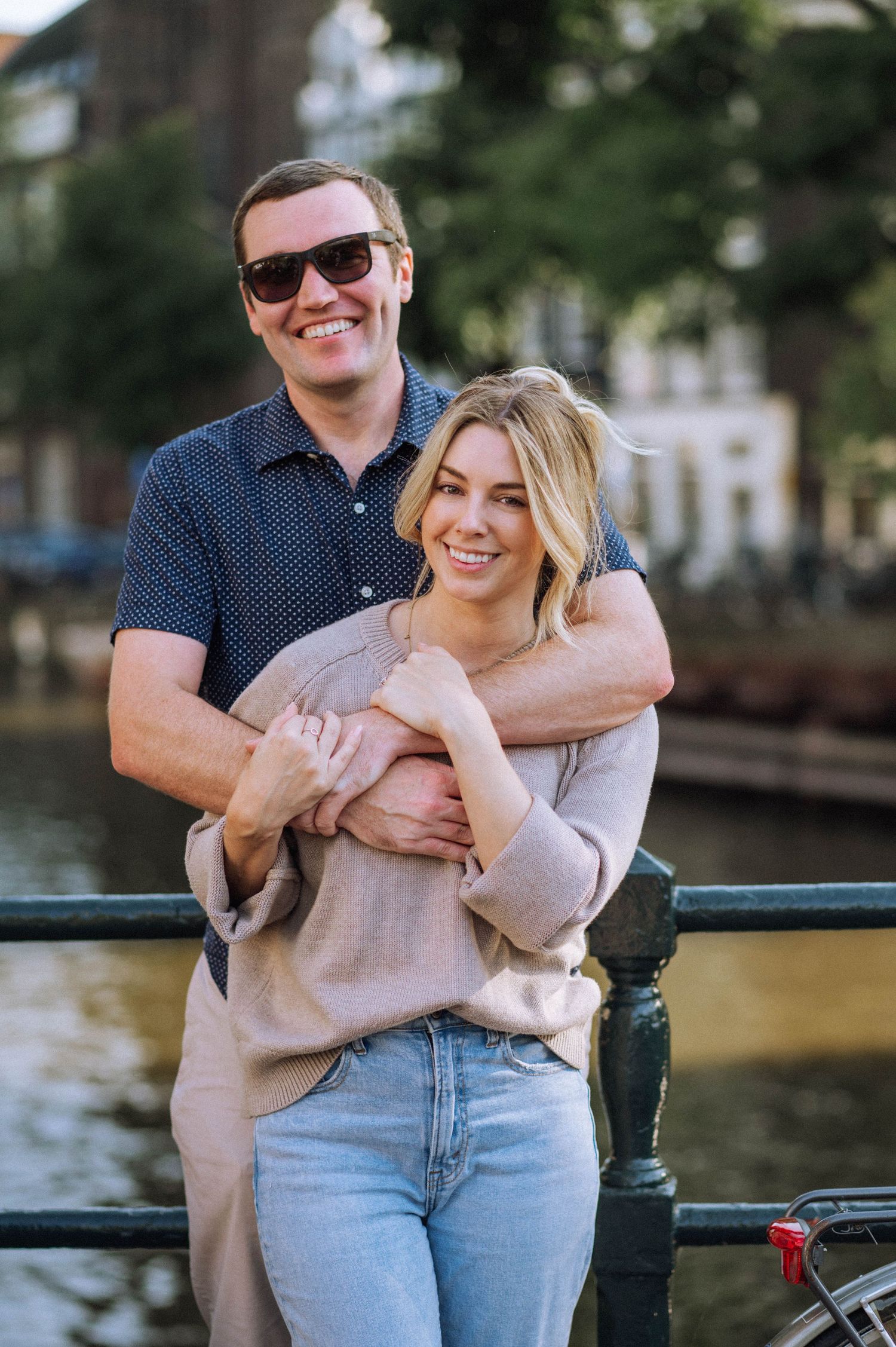 A candid shot of the couple laughing while strolling along a picturesque Amsterdam canal.