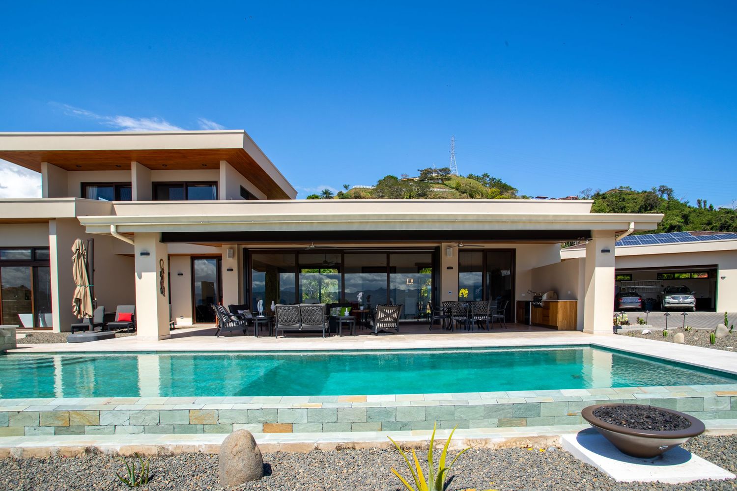 Daytime view of a modern luxury home with a swimming pool and open design, surrounded by greenery
