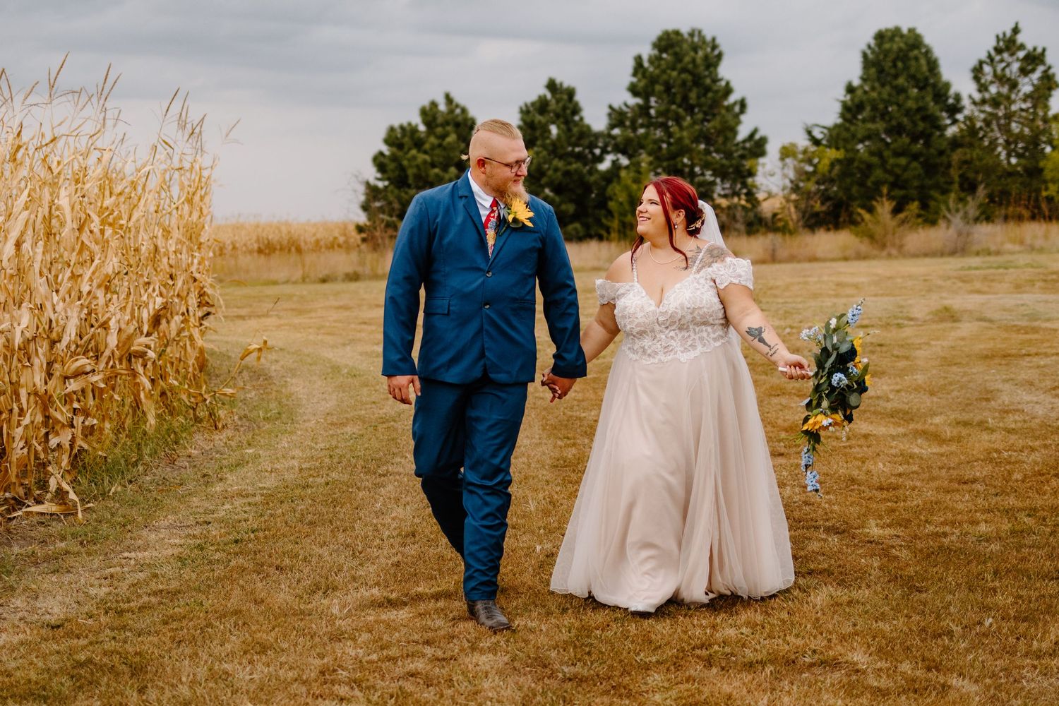 Couple walks hand in hand through a cornfield on their wedding day.