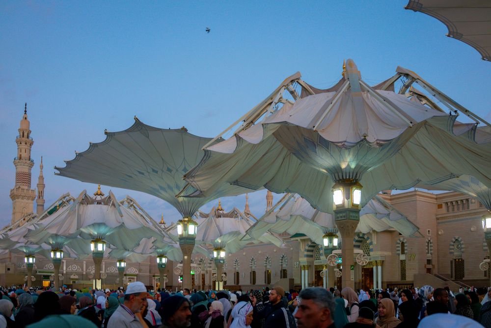 Large retractable umbrellas illuminate the courtyard of Masjid Al-Nabawi mosque in Medina during evening prayers.