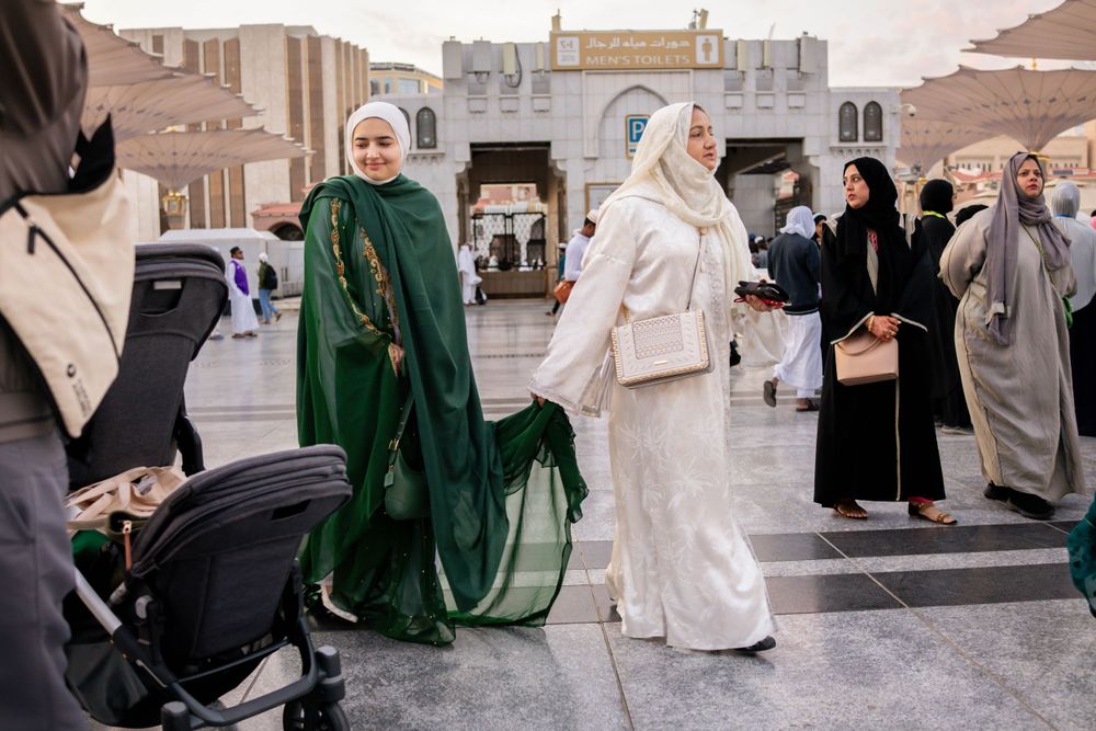 People wearing traditional Middle Eastern attire gather outside in an urban setting near traditional architecture.