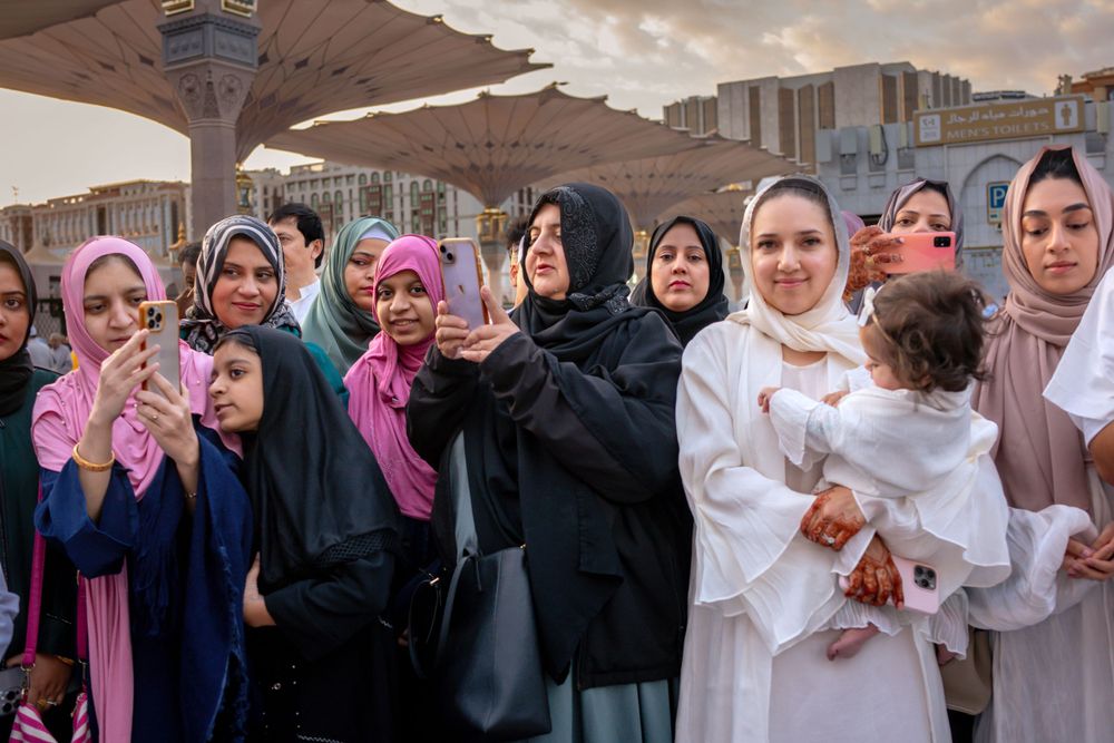 Group of people in traditional attire gathered under geometric umbrellas at Al-Masjid al-Nabawi mosque in Medina.