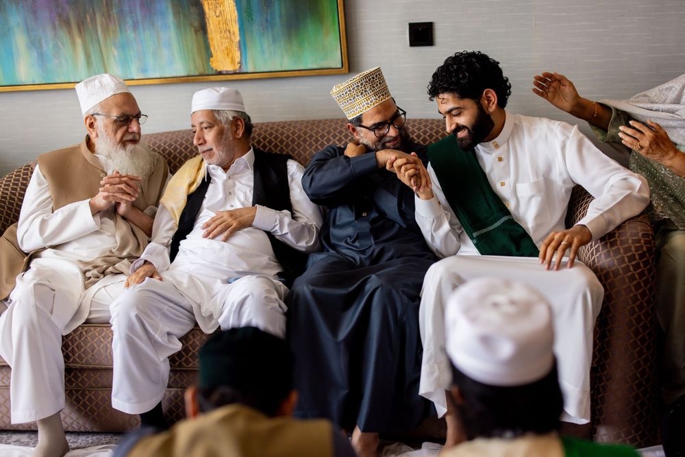 A group of men in traditional Middle Eastern attire share a joyful moment while sitting together on a couch.