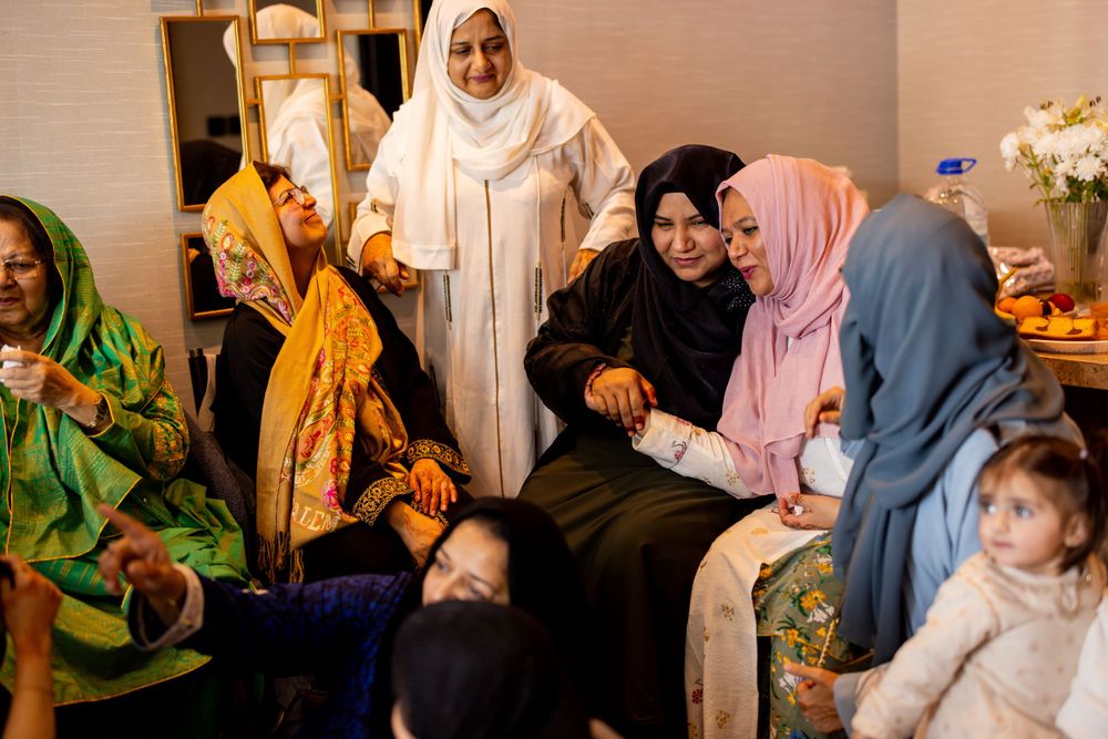 A group of people wearing colorful traditional clothing and hijabs gather together in an indoor setting at a social function.
