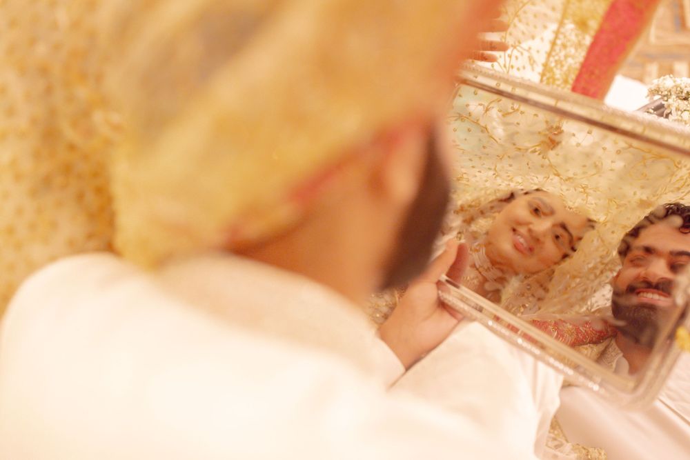 A person in blurry focus looks into a decorative mirror on the wall with a golden hue.