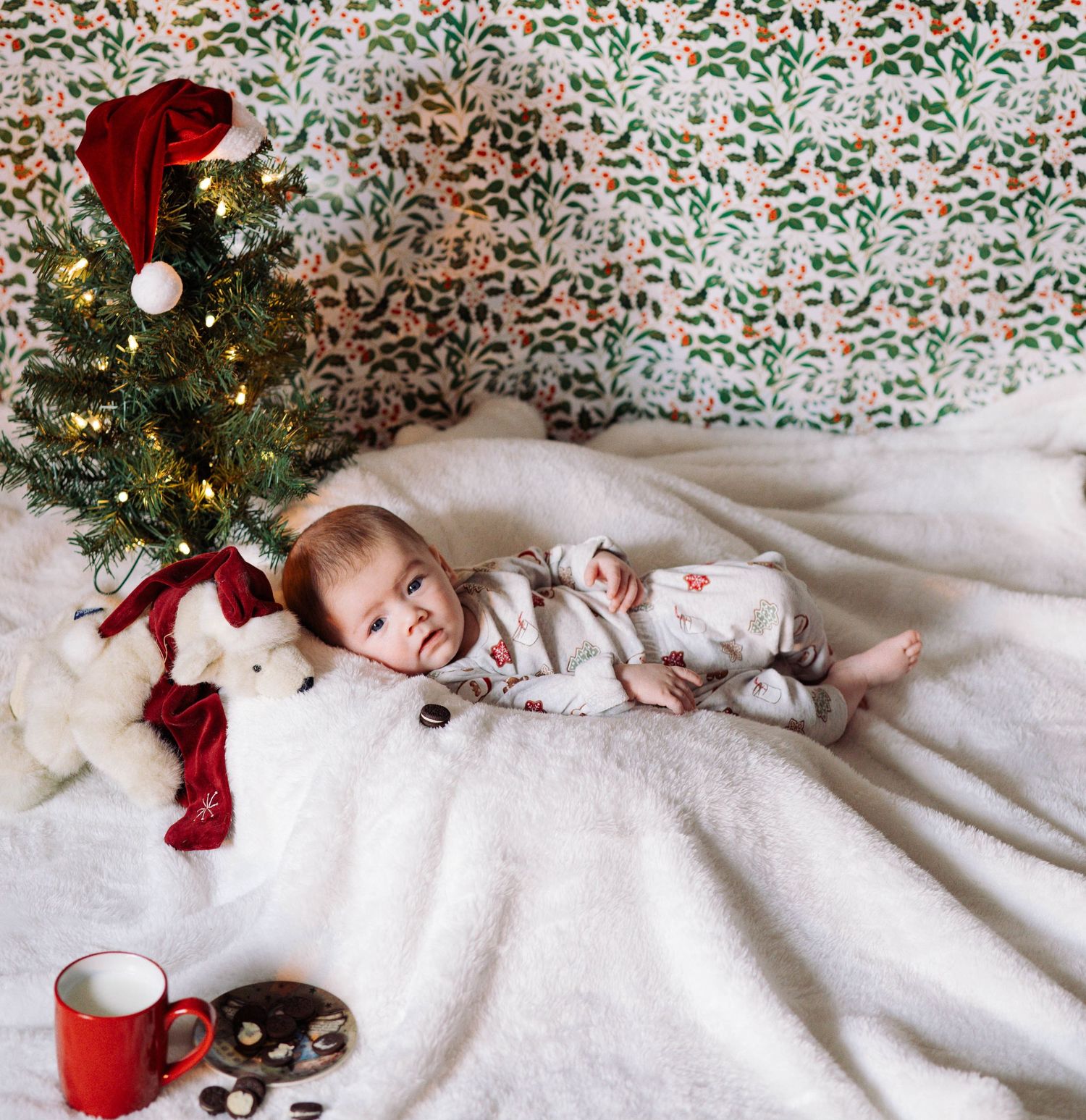 Baby lying on pink blanket wearing floral print dress with hand near face.