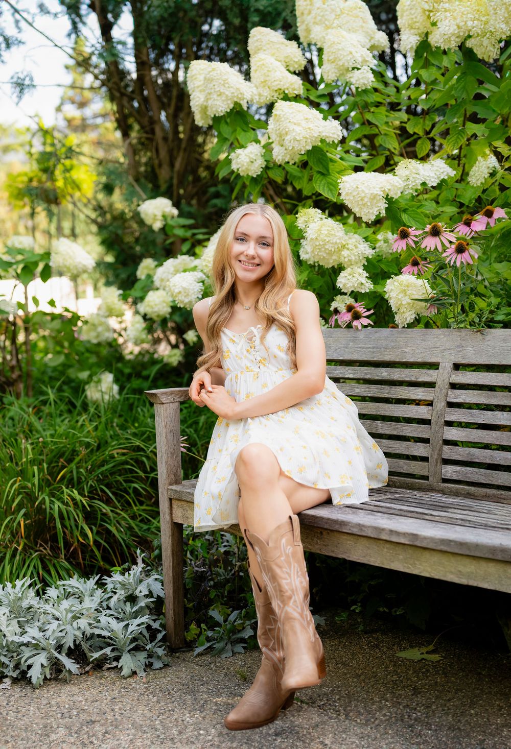 A white sundress and cowboy boots outfit styled against a garden bench with hydrangea blooms.