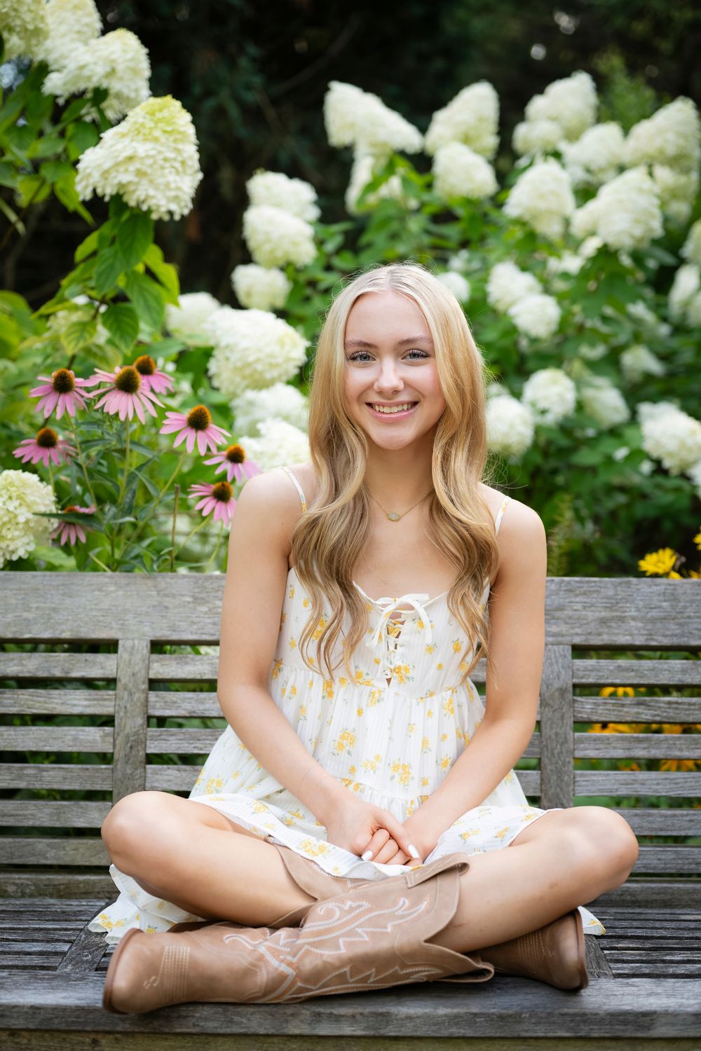 Summer portrait on wooden bench surrounded by white hydrangeas and purple coneflowers.