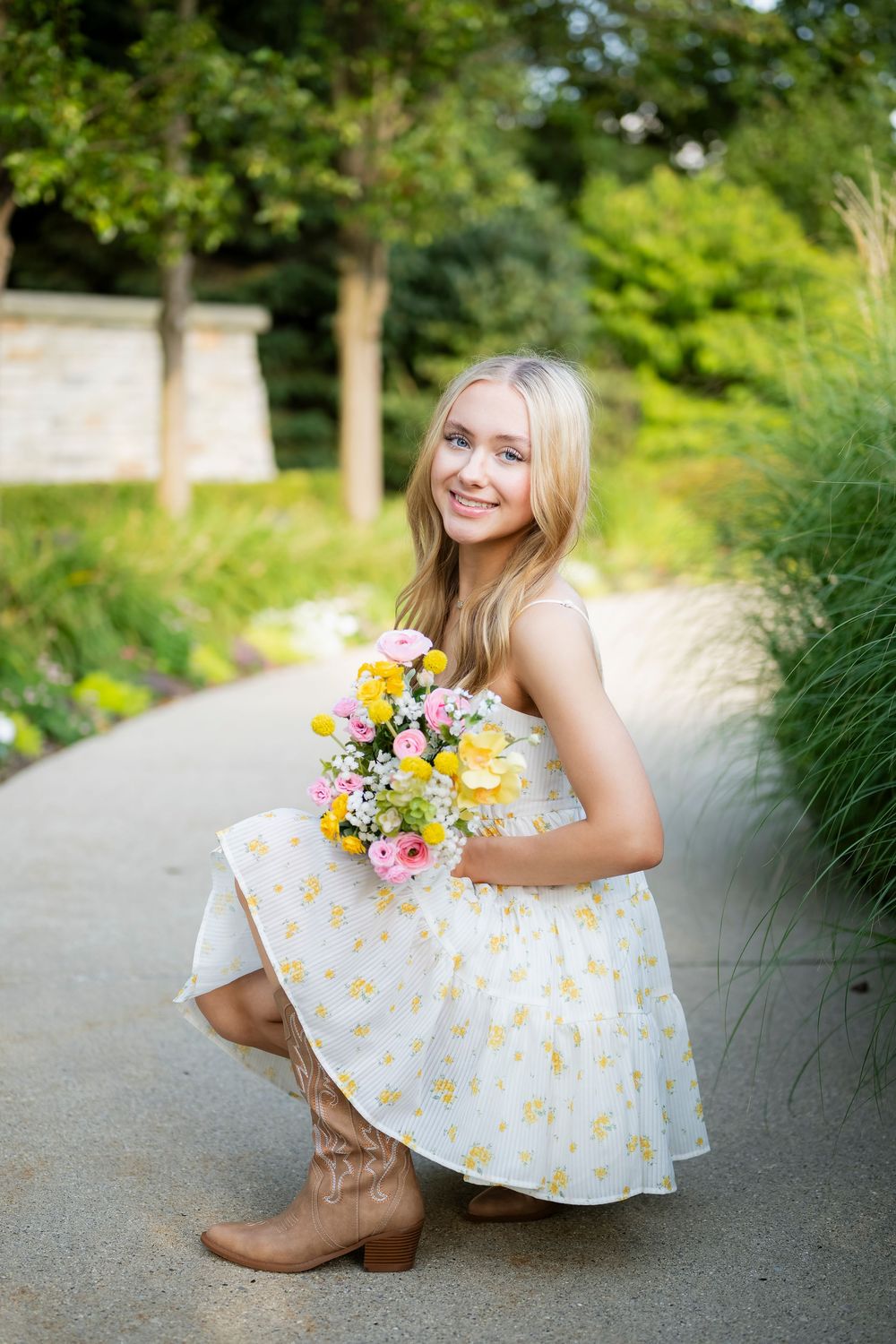 Summer portrait in a daisy print dress with wildflower bouquet on a garden path.