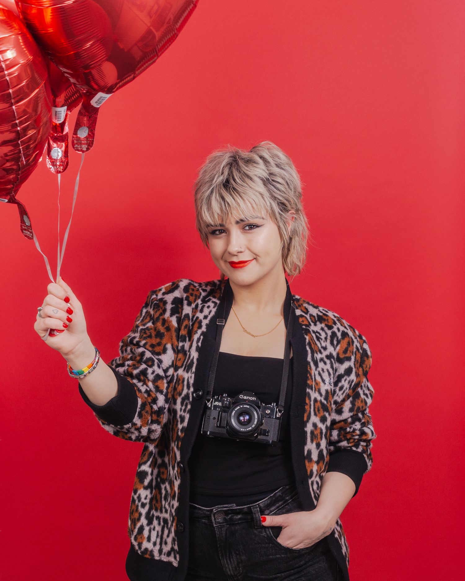 Person in a leopard print jacket holds red heart balloons against a vibrant red background.