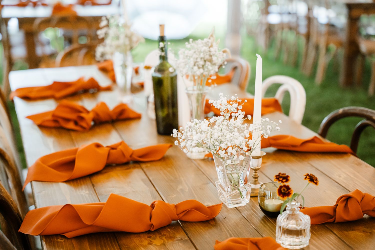 Rustic wooden table set with bright orange napkins and glassware for a wedding reception.