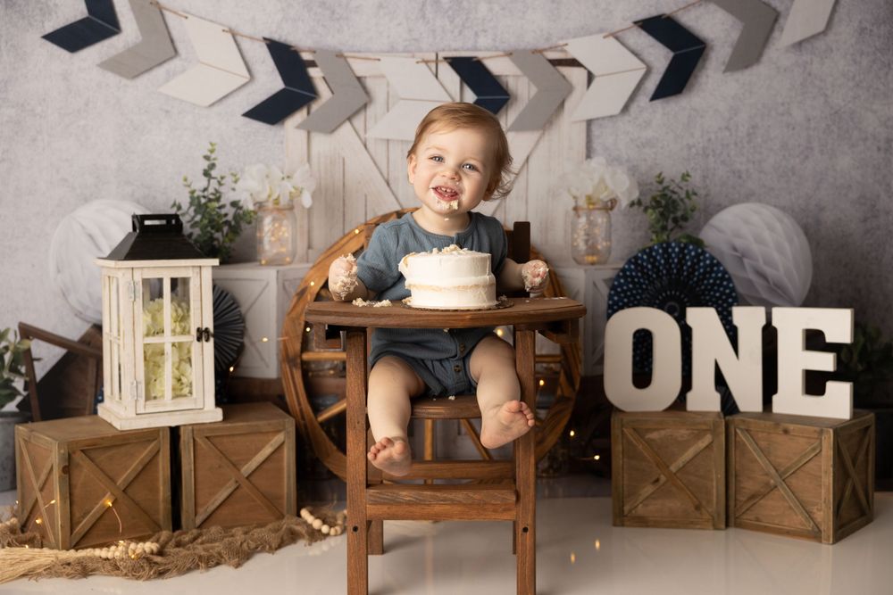 First birthday celebration setup with wooden decor, lantern, and small child sitting in wooden high chair with cake.