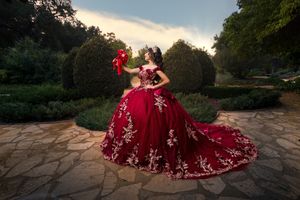 A stunning red ball gown with white floral embellishments photographed in a garden setting at dusk.