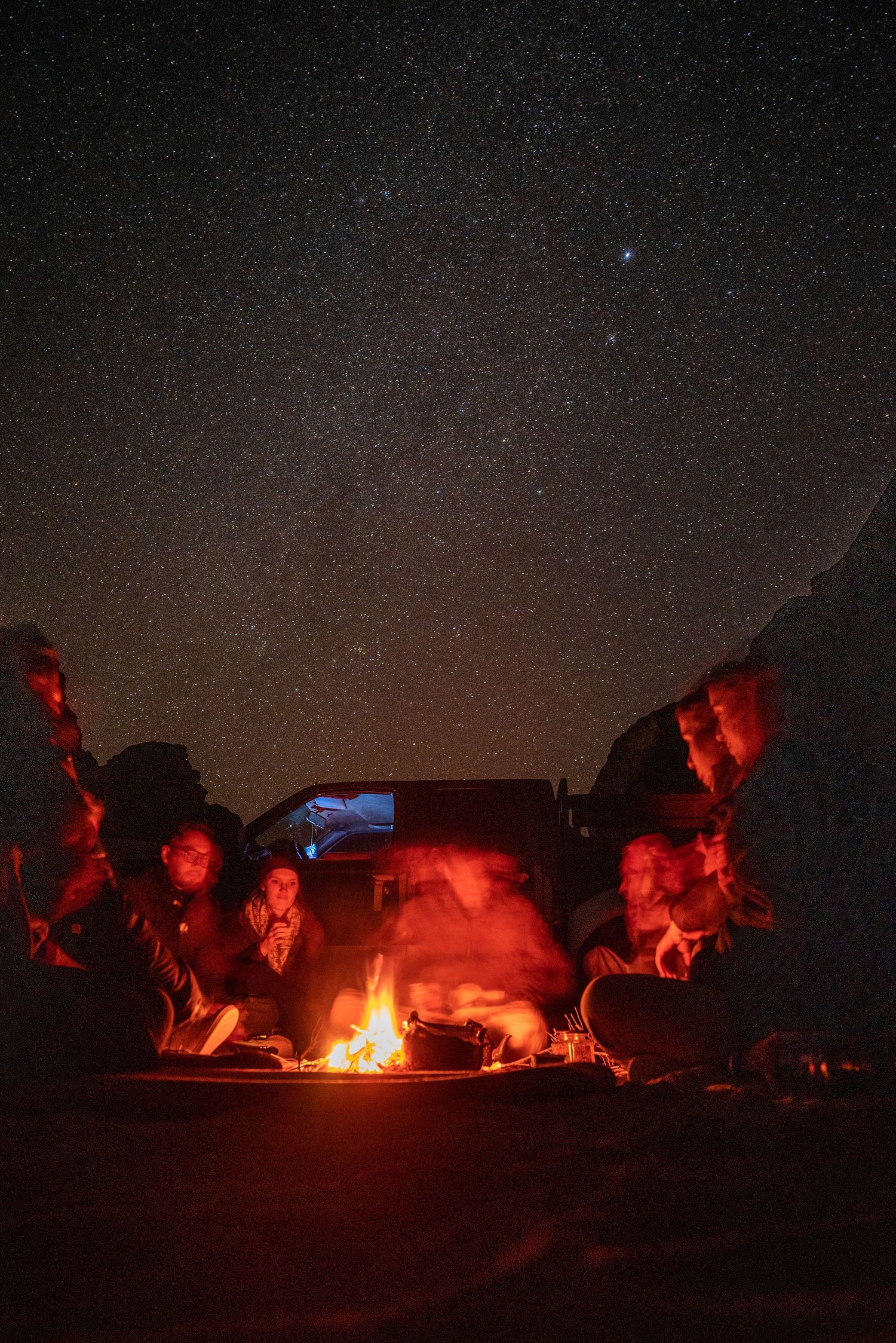 Campfire gathering under starry night sky with red-lit rock formations.
