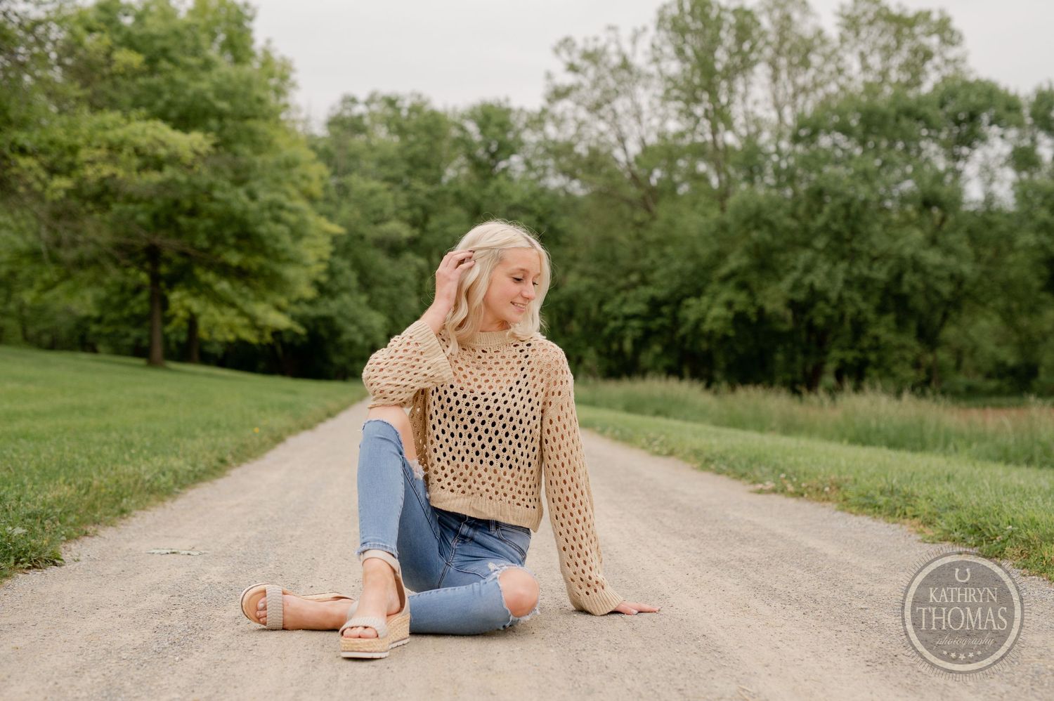 Candid outdoor photo on a gravel road wearing distressed jeans and a beige crochet top.