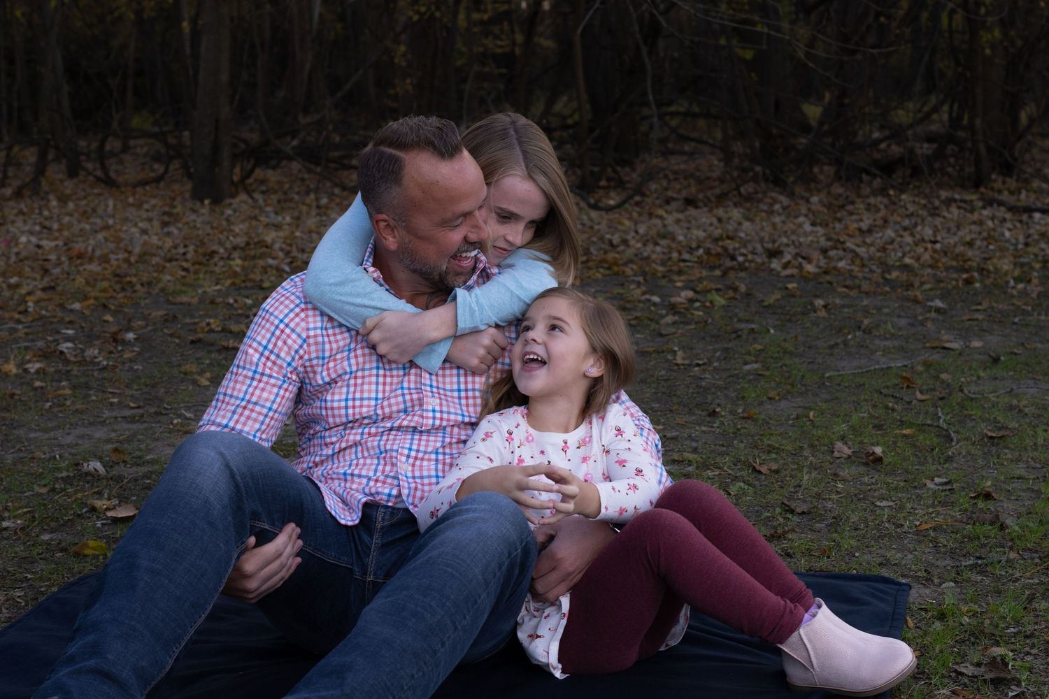 A family laughs together while sitting on the ground during an outdoor photo session.