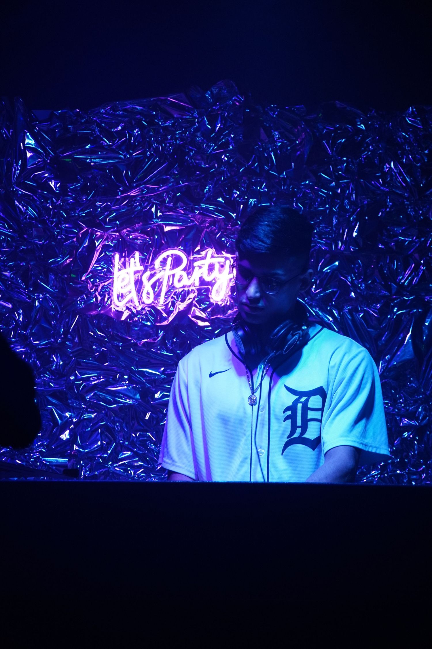 Person in Detroit Tigers jersey against blue metallic backdrop with neon party sign.