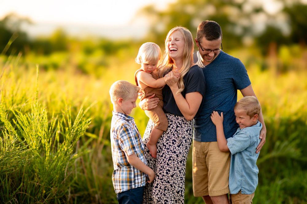 A family wearing casual attire shares joyful laughter together in a sunlit meadow during golden hour.