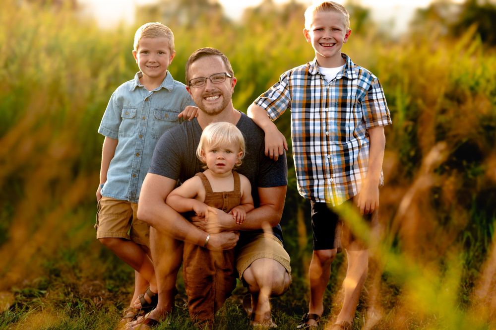 A group poses together in a golden field at sunset with tall grass surrounding them.