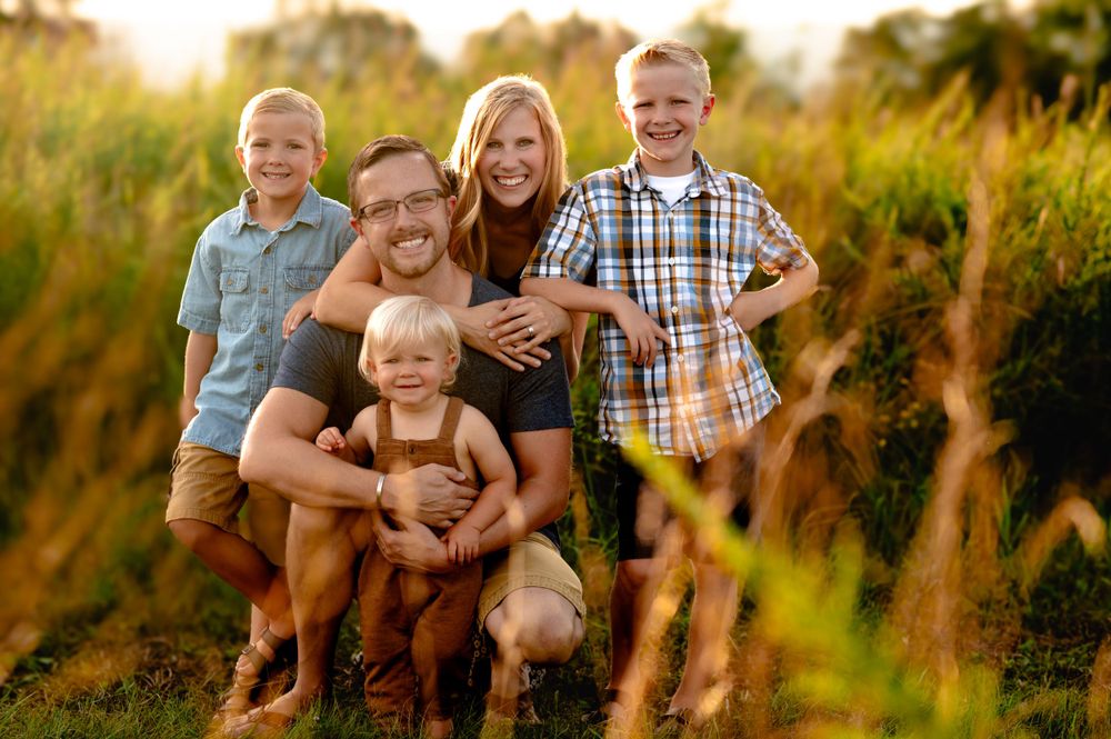 A loving family portrait captured in a golden sunlit field with tall grass during sunset.