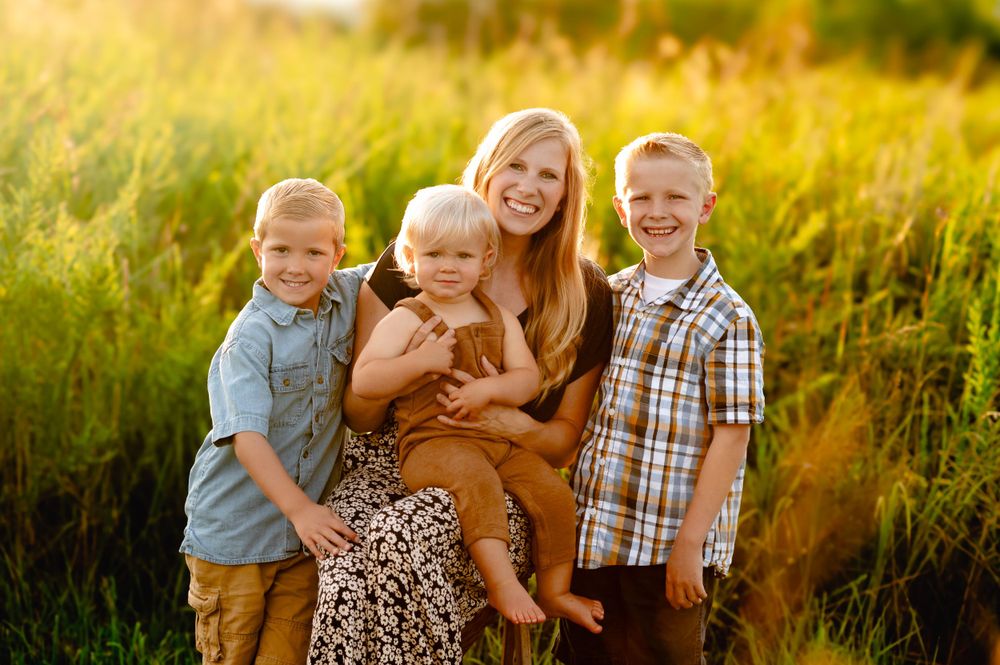A family group poses together in a sunlit meadow at golden hour, surrounded by tall grasses and warm summer light.