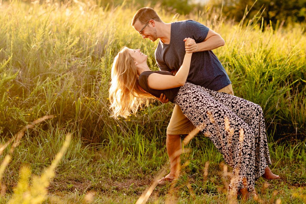 A couple shares a romantic moment dancing together in a sunlit meadow at golden hour.